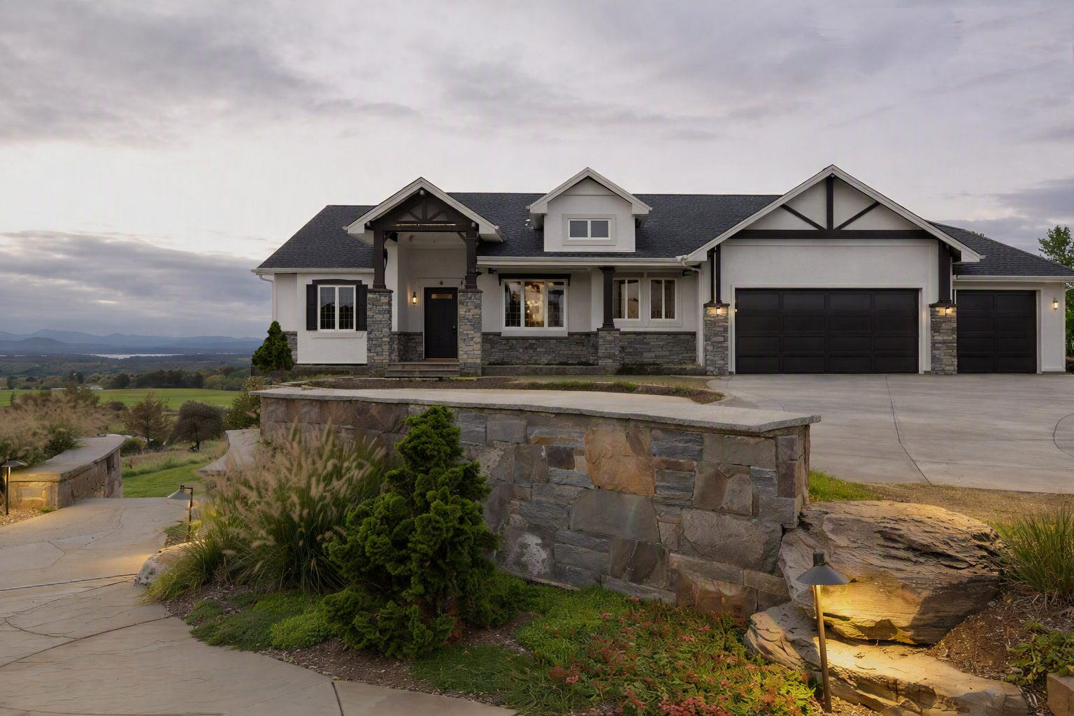 Telluride II ranch home concept at dusk on a hilltop above a valley lake, with stone retaining walls and mountain ridges beyond